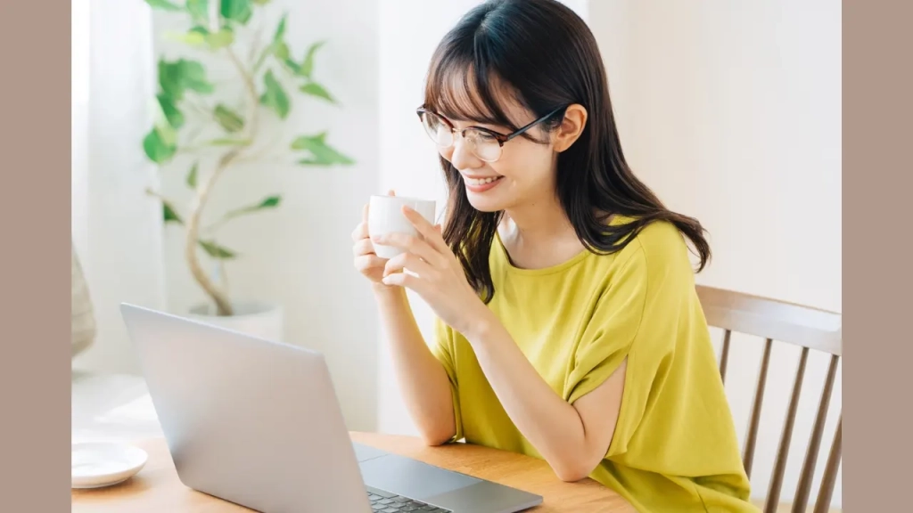 コーヒーを片手にPCを見ている女性。